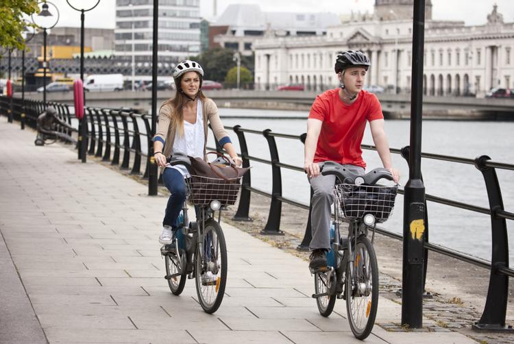 Two people cycling along the River Liffey in Dublin city center, a short distance from The Trinity City Hotel.
