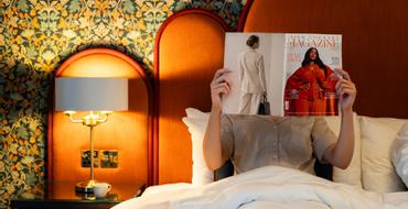 A woman with a magazine on a bed with a cup of coffee inside a Georgian Suite at The Trinity City Hotel, Dublin.